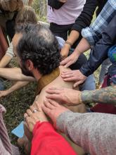 Rev. Prakasa kneels to deliver a blessing to the Naropa M. Div cohort